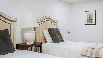 Une chambre d’hôtel avec deux lits, une table de chevet avec une lampe, une porte et un tableau encadré au mur.