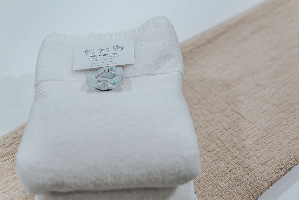 A neatly folded white towel with a tag that reads 'Enjoy your stay' and 'Need something? Text us.'