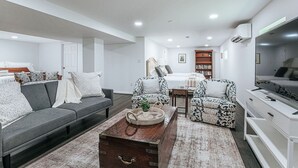 A modern living room with a sofa, armchairs, a coffee table, a TV, and a bookshelf. - Cavalier Cocoon (Charlottesville)