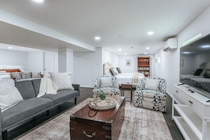 A modern living room with a sofa, armchairs, a coffee table, a TV, and a bookshelf. - Cavalier Cocoon (Charlottesville)