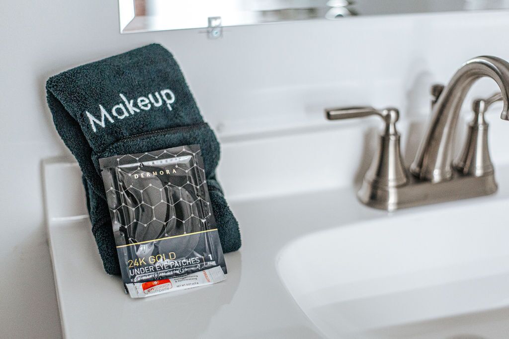 Een wastafel in een badkamer met een handdoek waarop 'Make-up' staat en een pakje Dermorix 24K Gold Onder-Oog pleisters.