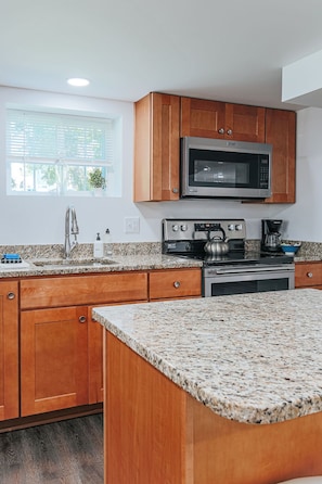 A kitchen with wooden cabinets, a stainless steel microwave, a stove, and granite countertops.