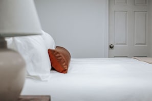 A neatly made bed with white bedding and a single brown pillow.