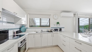 Una cocina moderna con armarios blancos, horno empotrado, microondas, fregadero y ventana con vistas.