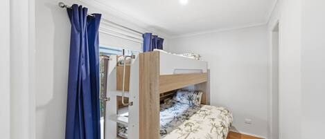 Una cama litera con estructura de madera, pared blanca y ventana con cortinas azules.