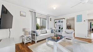 Un salon moderne avec un canapé, une table basse et un téléviseur. On y trouve également une bibliothèque et une fenêtre avec des rideaux.