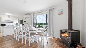 Une cuisine moderne avec des meubles blancs, un coin repas avec des chaises blanches et un poêle à bois.