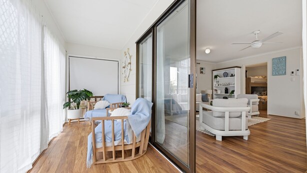 Un vaste espace de vie doté d’une porte-fenêtre coulissante, d’un plancher en bois, d’un canapé blanc, d’une chaise en bois et d’une bibliothèque blanche.