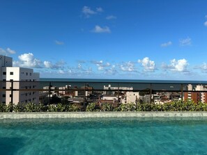 Ein klarer Blick auf einen Swimmingpool, im Hintergrund Stadtansicht und Meer.