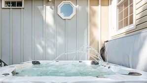 Un jacuzzi con chorros de agua, rodeado por una terraza de madera y una casa con ventana y puerta.