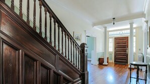Una imponente escalera con balaustres de madera oscura y un suelo de madera pulida que conduce a una habitación con un gran ventanal y una puerta de paneles de madera.