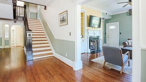 Un amplio espacio de sala con pisos de madera, una escalera con barandilla de madera oscura y un sillón gris.
