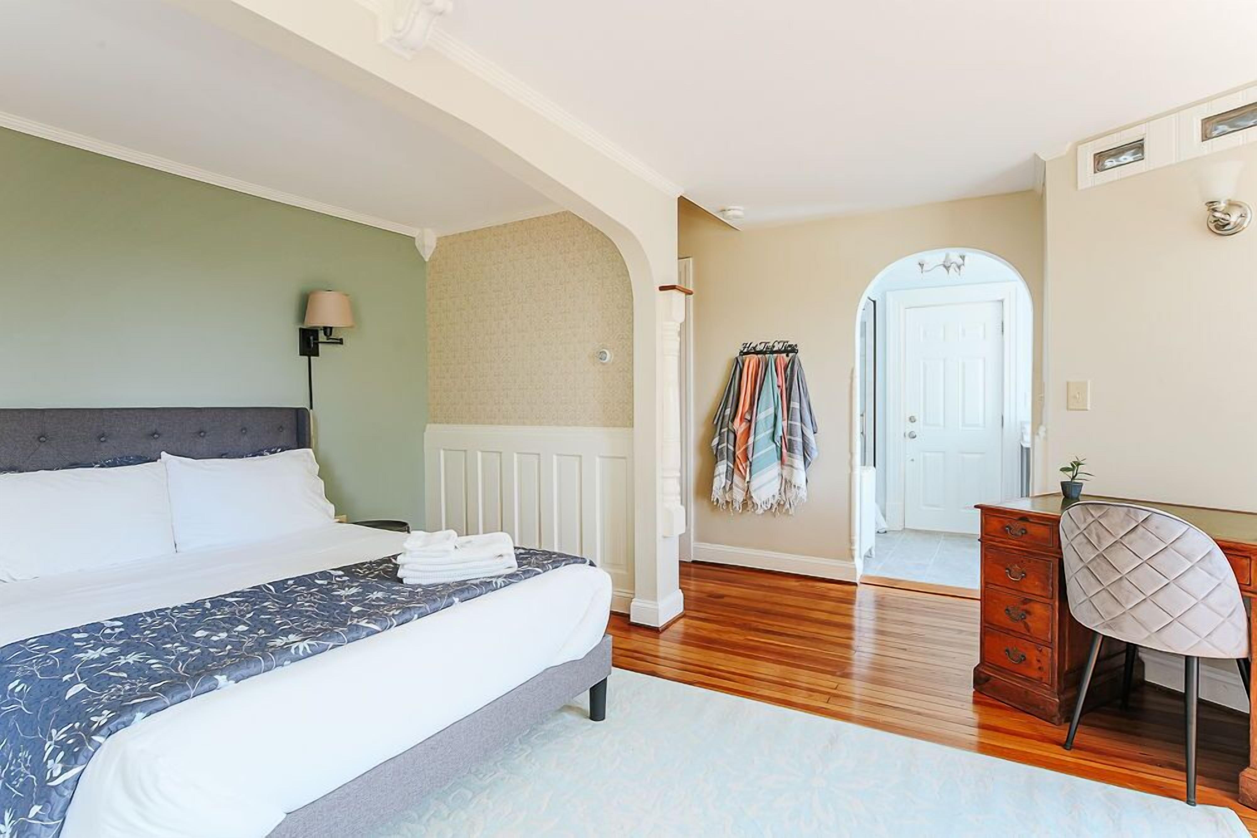 Un dormitorio con una cama grande, un aparador, una silla y una puerta que da a otra habitación.