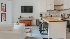 A modern kitchen with white cabinets, a wooden island, and a flat-screen TV mounted above the counter. - Daydream & Draft (Staunton)