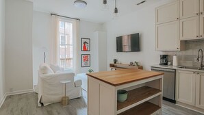 A modern kitchen with a wooden island, white cabinetry, a flat-screen TV, and a dining area with a white sofa and table. - Daydream & Draft (Staunton)