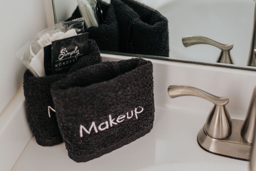 A bathroom with a mirror, a sink, and a black towel rack holding a towel labeled 'Makeup'.