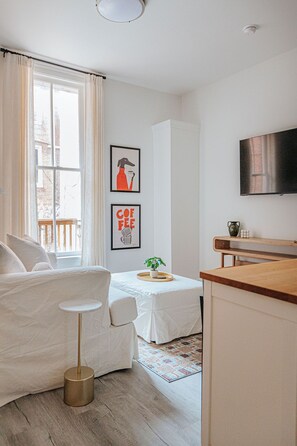 Una sala de estar moderna y minimalista con un sofá, una mesita, una mesa de centro, un televisor y una ventana con cortinas.