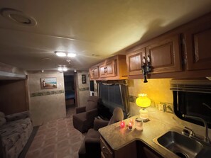 A compact RV kitchen with wooden cabinets, a sink, a dining area with a table and chairs, and a small seating area with a couch. -  The SeaNote, Kitty Hawk, NC-- A tranquil stay located just 5 minutes from beach (Kitty Hawk)
