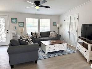 Ein Wohnzimmer mit grauem Sofa, Couchtisch, Fernsehschrank und Deckenventilator.