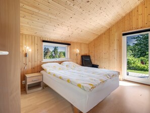 Ein Schlafzimmer mit Holzwandverkleidung, einem Bett, einem Nachttisch und einem Fenster mit Blick auf Grünflächen.