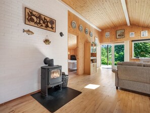 Ein gemütliches Zimmer mit Kaminofen, einer Couch und einem Essbereich mit Holzwänden und einem Kamin aus Ziegelsteinen.