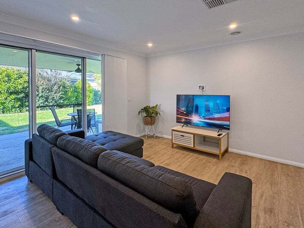 Un salon moderne avec un grand téléviseur à écran plat, un canapé de couleur foncée, un petit meuble télé en bois et une plante en pot.