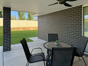 Een terras met een glazen tafel en stoelen, een plafondventilator en een bakstenen muur.
