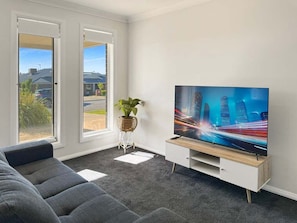 A modern living room with a large flat-screen TV, grey sofa, and a potted plant.