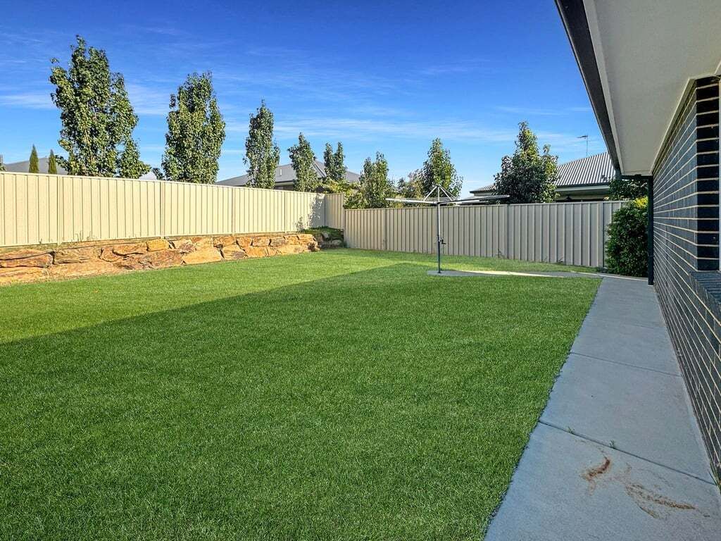 A backyard with a well-maintained lawn, a stone wall, and a wooden fence.