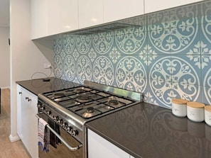 A kitchen with a gas stove, oven, and patterned backsplash.