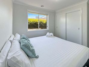 Un dormitorio con cama, almohadas, una ventana y una puerta.