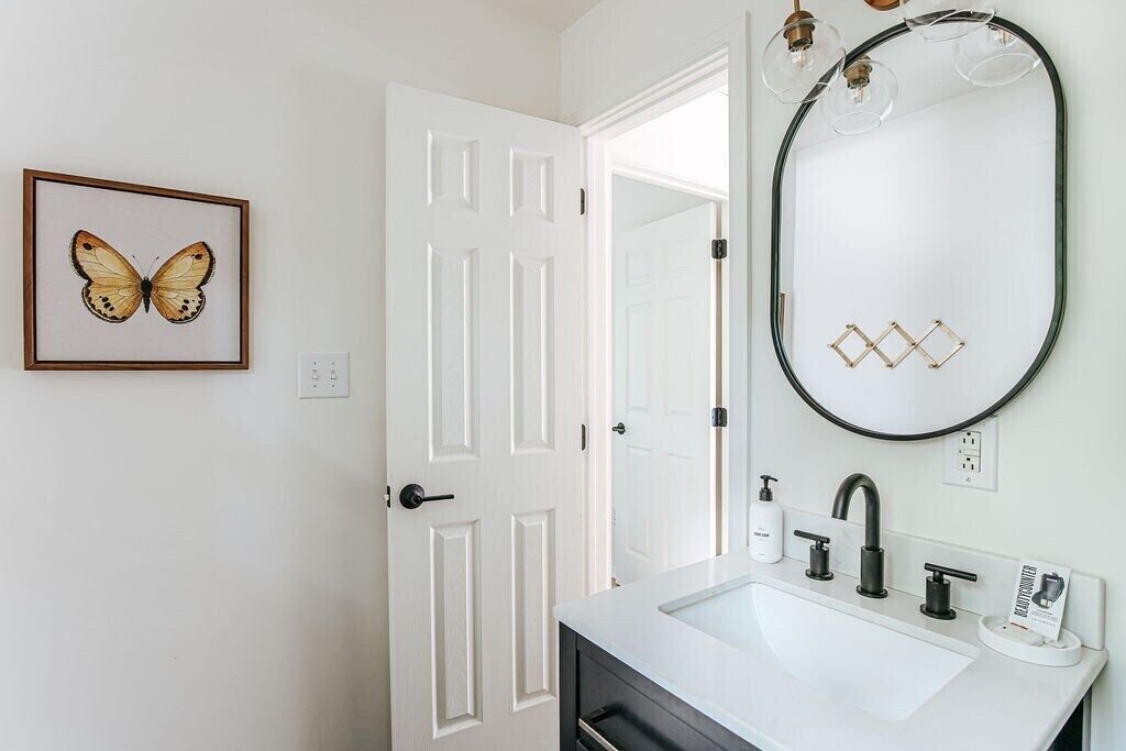 A bathroom with a white sink, black faucet, and a large oval mirror with a geometric frame.