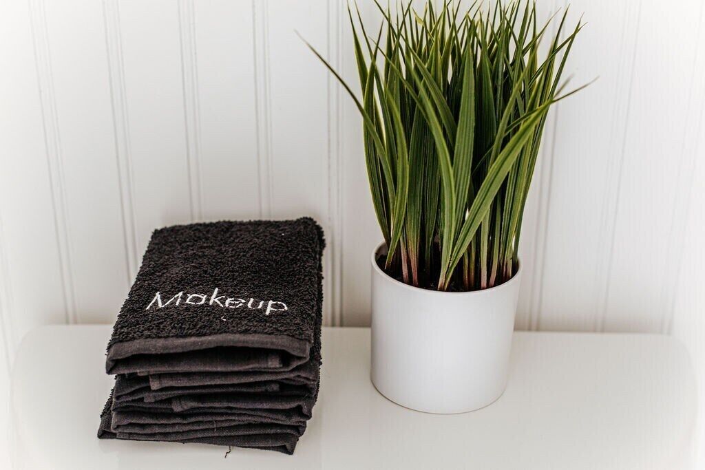 A stack of black towels with the word "Makeup" on them and a white pot with green plants.