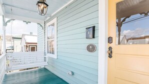 Eine Veranda mit einer Schaukel, eine Tür mit einer Nummertafel und ein Fenster mit einer Tafel.