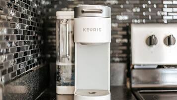Une machine à café Keurig blanche est posée sur un comptoir de cuisine, avec un dosseret de carreaux noirs.