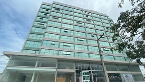A multi-story building with a glass facade, a central entrance with a glass door, and a parking area with several cars. - Bela Hospedagem - Wind Palace 606  (Cabedelo)