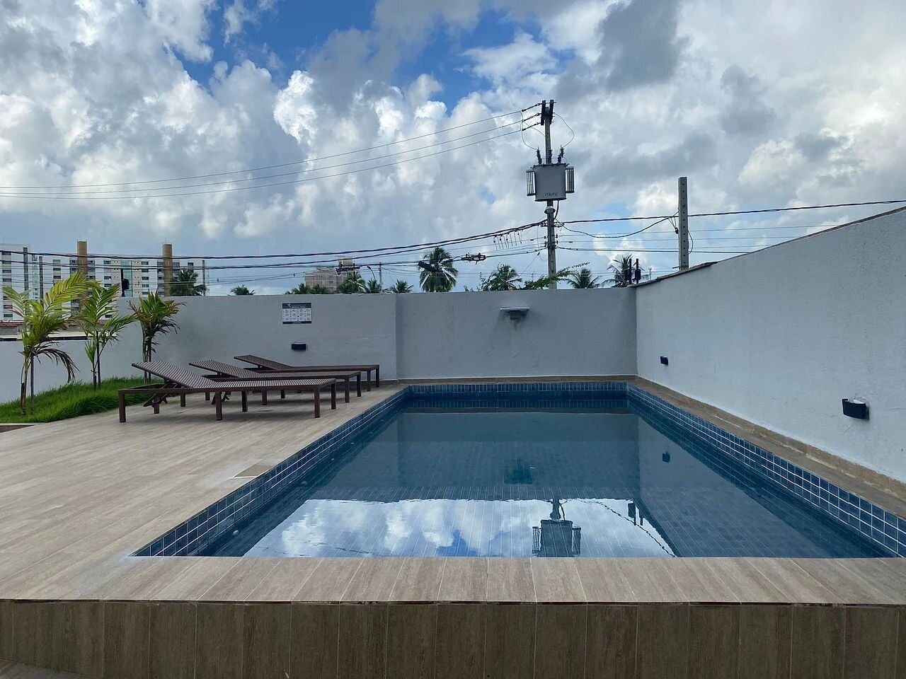 A rooftop swimming pool with a tiled edge, surrounded by a wooden deck and a few lounge chairs.