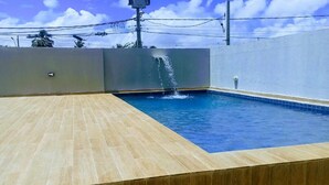 A swimming pool with a tiled deck, a water feature, and a utility pole in the background. - Bela Hospedagem - Wind Palace 606  (Cabedelo)
