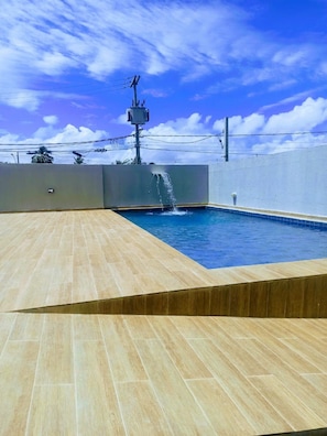 Ein Pool mit Fliesen umgeben, einer Wasserspiels und einem Strommast im Hintergrund.