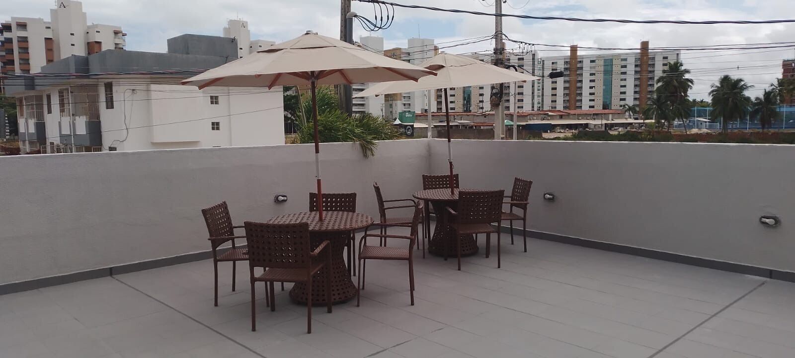 A rooftop terrace with a table and chairs, umbrellas, and a view of buildings in the background.