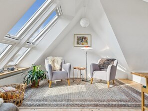 Ein Schlafzimmer im Loft-Stil mit Dachfenstern, einem großen Teppich, zwei Sesseln, einer Stehlampe und einem Gemälde an der Wand.
