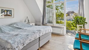 Una camera da letto con un letto, una scrivania, una sedia, un termosifone e una finestra che si affaccia su case e alberi.