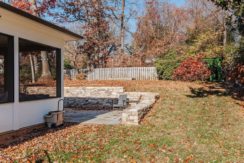 Un patio cubierto con escalones de piedra, un hogar para fogata y una cerca de madera en un jardín trasero.