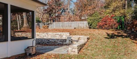 A covered patio with stone steps, a fire pit, and a wooden fence in a backyard.