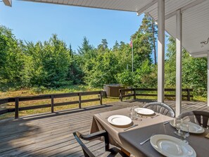 Une terrasse en bois avec une table dressée pour le repas, entourée d’un belvédère blanc et offrant une vue sur une zone boisée.