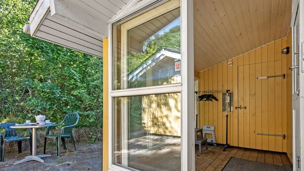 Fachada de madera con un gran ventanal, un pequeño espacio exterior con mesa y sillas, y una terraza de madera.