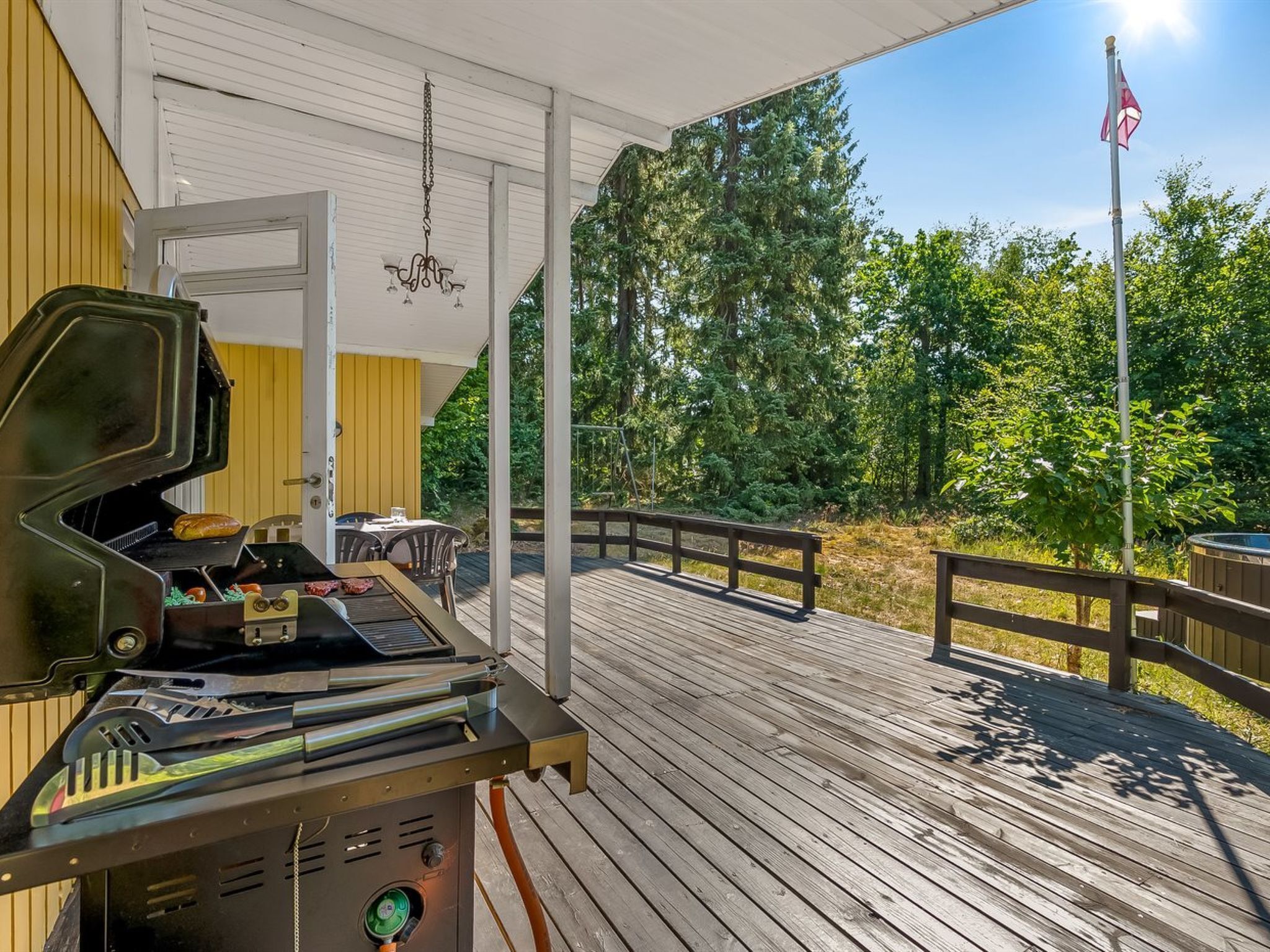 Ein überdachter Außenbereich mit Grill, Tisch mit Stühlen und einer Holzterrasse.