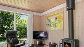 Una habitación acogedora con techo de madera, un sillón de cuero negro, un televisor y una estufa de leña.