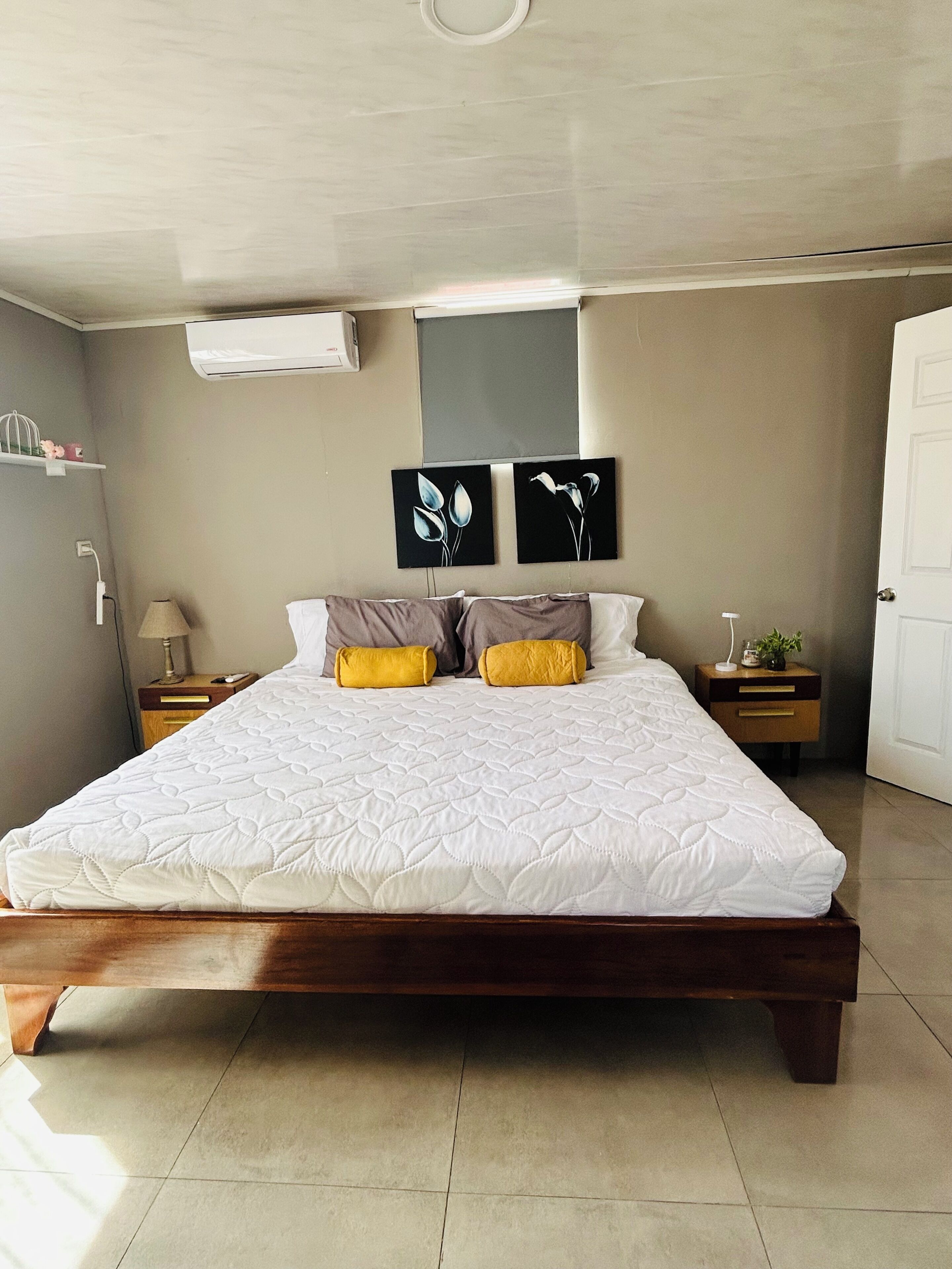 A bedroom with a bed, two wall-mounted paintings, a bedside table with a lamp, and a door.. Einoah Apartment Private, Safe and Close to Everything