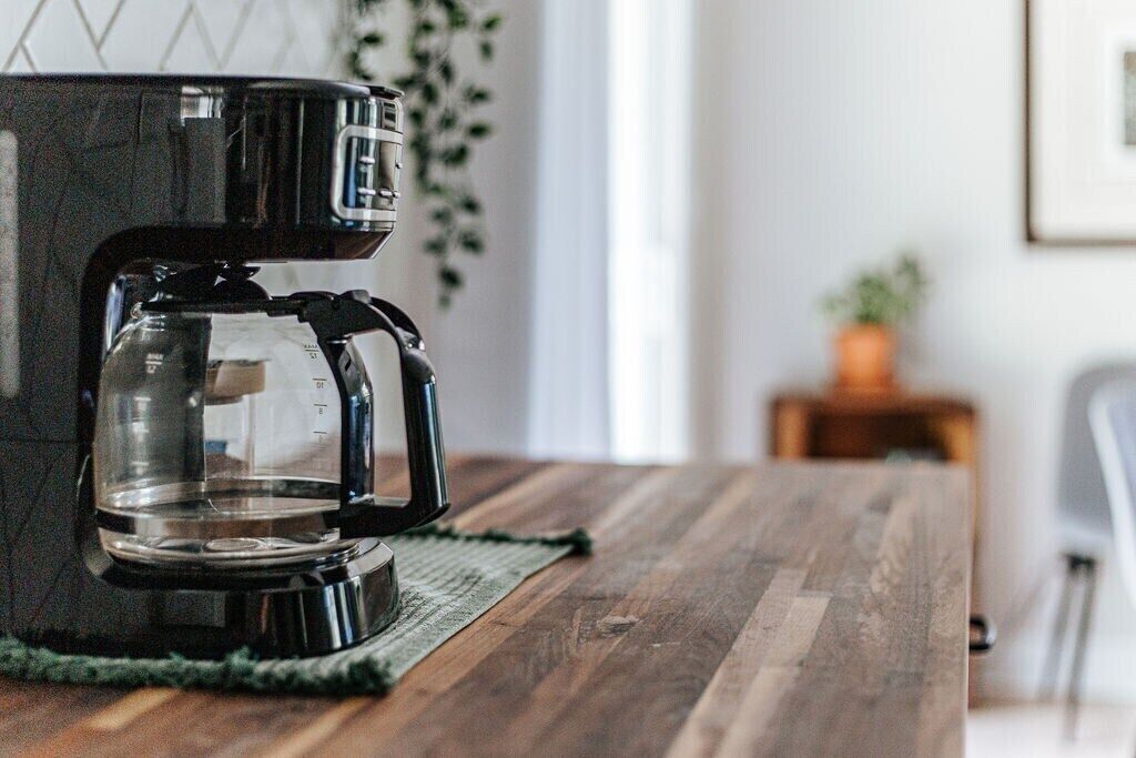 Una cafetera sobre una mesa de madera con un posavasos verde.